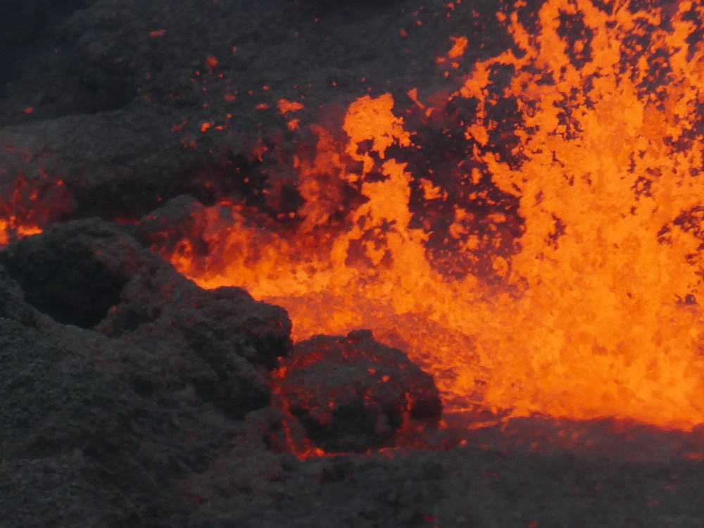 An extreme close-up of flying lava (taken with my good zoom, not by getting this close!). It's very orange and in the foreground is something that looks like a boulder that looks like it's made of fire.