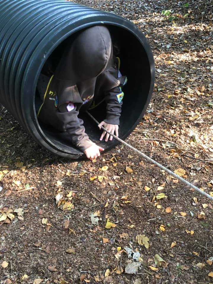 A Brownie even I can't identify, wearing her uniform hoodie backwards as a blindfold, crawls out of a tunnel during the Night Line activity