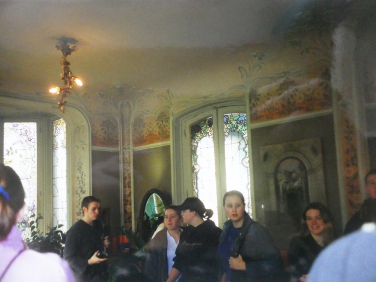 Several of our school group standing around in an opulent room with floral wallpaper and Art Nouveau stained glass windows. This is Louis Vuitton's house and we're about to be served champagne after a tour of the factory.