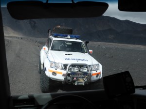 An Icelandic police car - actually, a 4x4 mountain patrol car - in the grey gravelly desert of the Highlands, as seen from the front seat of our big jeep.
