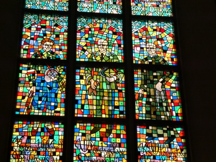 Modern figures from Polish politics, art & religion in mosaiced stained glass.