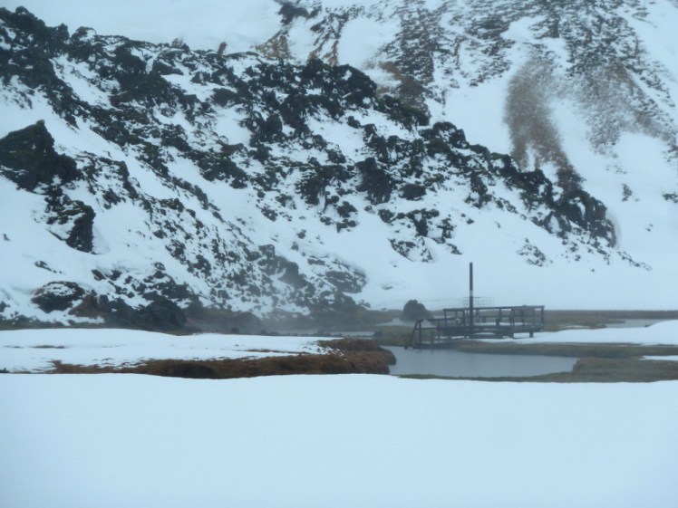 The hot spring: a steaming natural pool, the snow around its edges melted by the heat. Everywhere else is thick snow and behind it is the edge of the 500-year-old lava field, with jagged lava sticking out of the snow trying to coat it.