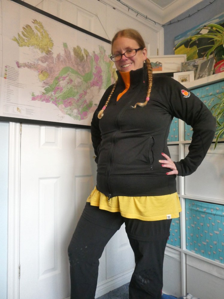 Same place, same hair etc. Now I'm wearing a black jacket with an asymmetrical zip. The collar has a large orange triangular insert so I can cover part of my face when it's zipped to the top. A yellow top is escaping the bottom of the jacket.