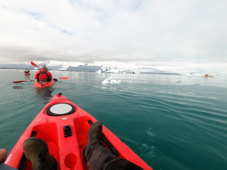 My feet in my kayak again. Ahead of me is a line of paddlers in red buoyancy aids & jackets which contrast really well with the turquoise and white of the lake water and ice.