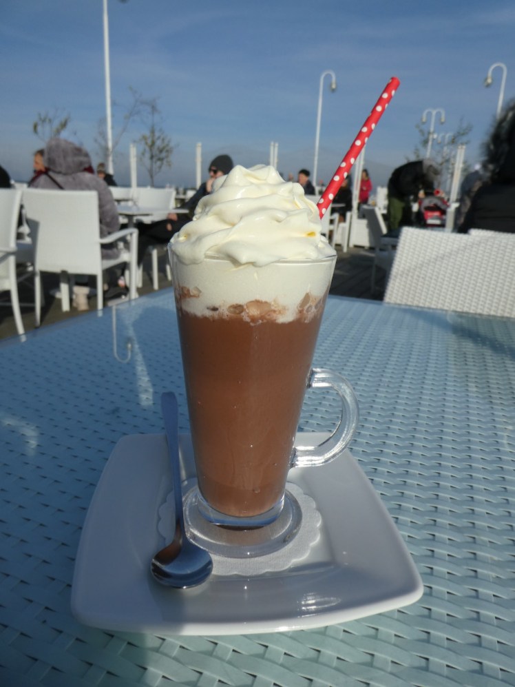 Hot chocolate in a tall sundae glass with a mound of cream on top.