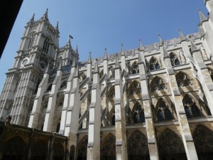 The south side of Westminster Abbey as seen from the cloisters; a mass of white Gothic architecture with tall buttresses, shadowed slightly the cloister wall on the left.