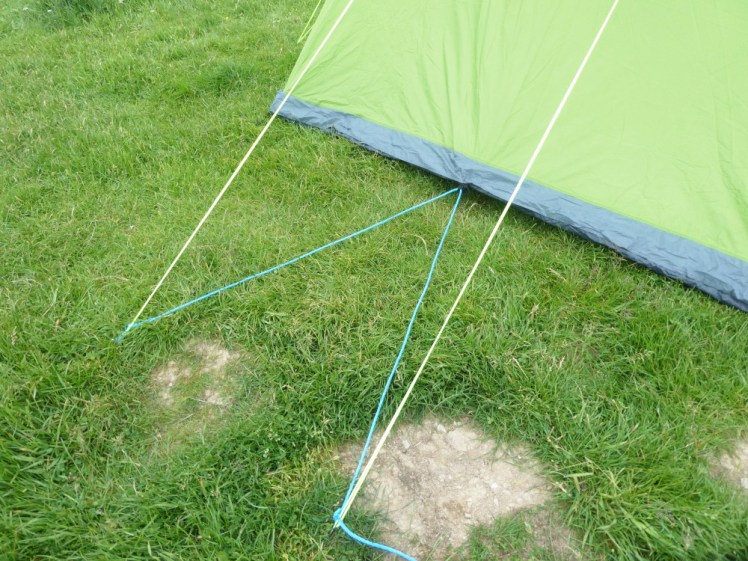 A length of blue agricultural rope being used as an improvised peg. It runs from one peg to the other via the loop on the bottom edge of my tent, where the ground is too stony to get an actual peg in.