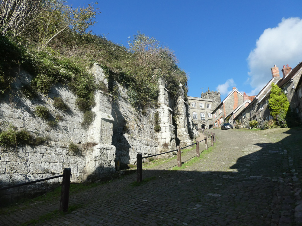 Gold Hill looking upwards, with that bright sun on the overgrown buttressed stone walls that are holding up the abbey grounds.
