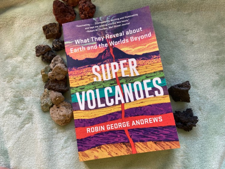 Super Volcanoes by Robin George Andrews, lying on a pale green blanket and surrounded by my volcanic rock collection.