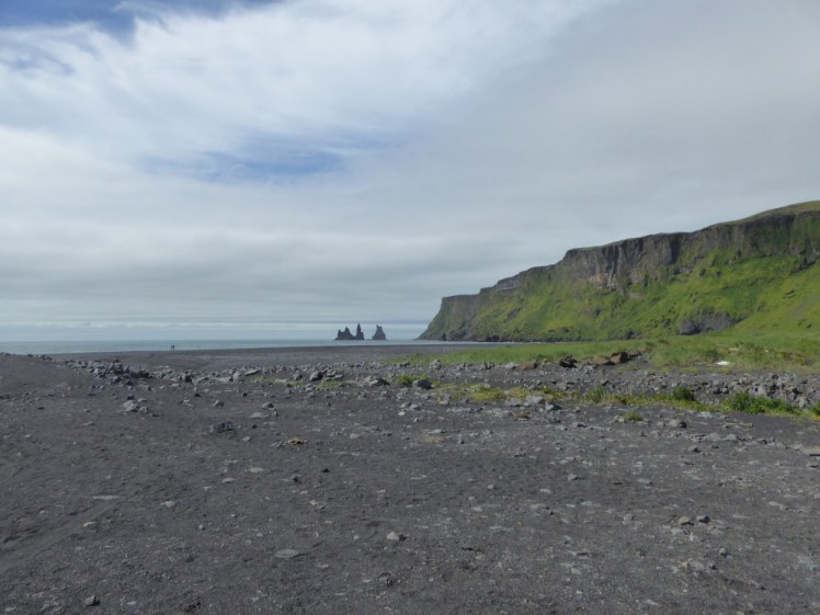 The grey sand beach at Vik, with a green mossy mountain descending into the water and jagged pinnacles sticking up out of the water. No restaurants in sight.