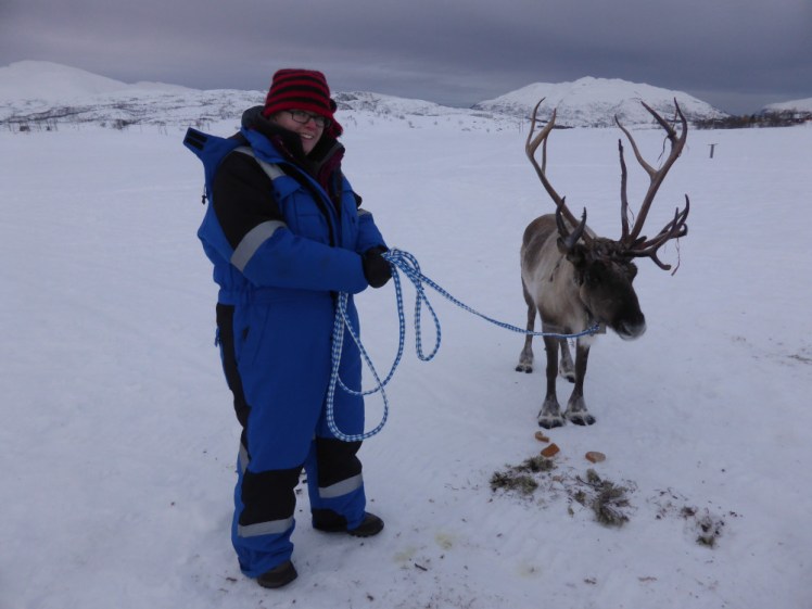 Me in a blue padded snowsuit holding a rope loosely attached to a reindeer who just does not care.
