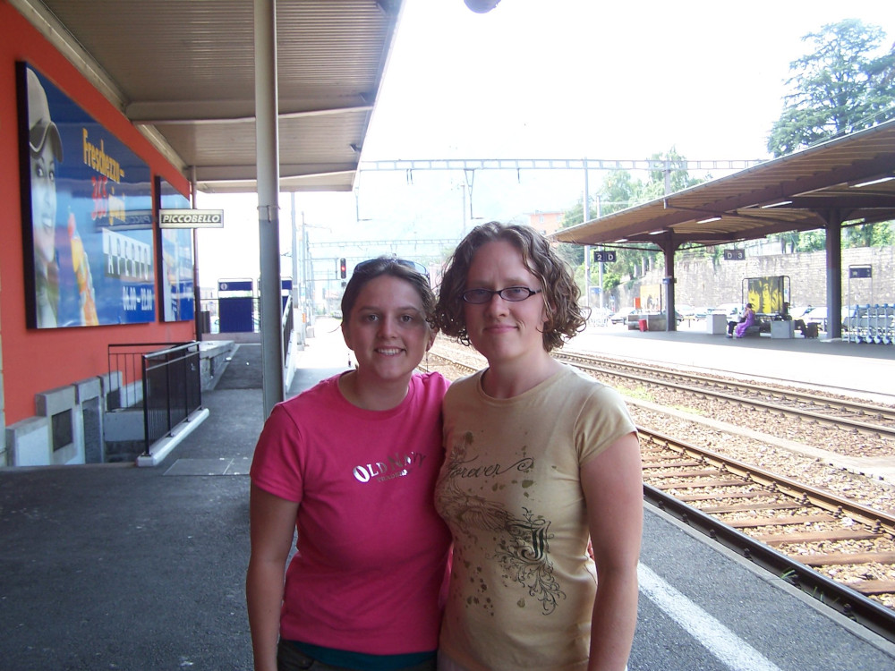 Jemma, in a pink t-shirt and Angela in a light yellow one posing for the camera at a station which I presume is Lugano. It's sunny.