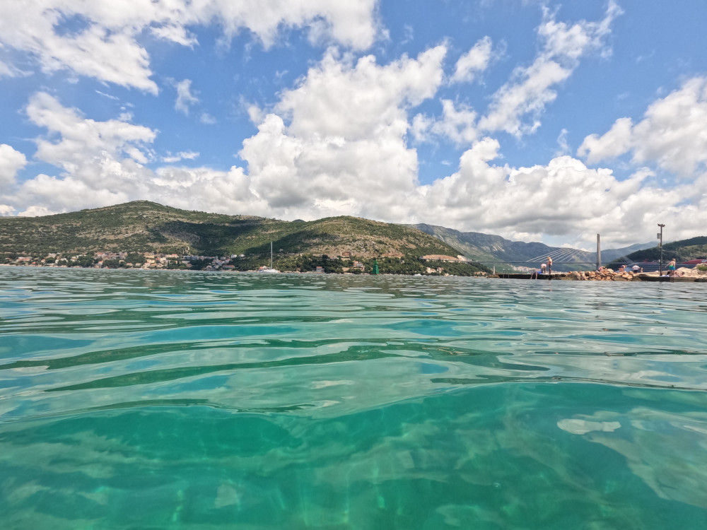 Looking across the port, with crystal-clear greenish-blue water, to the Dubrovnik bridge and the mountains.