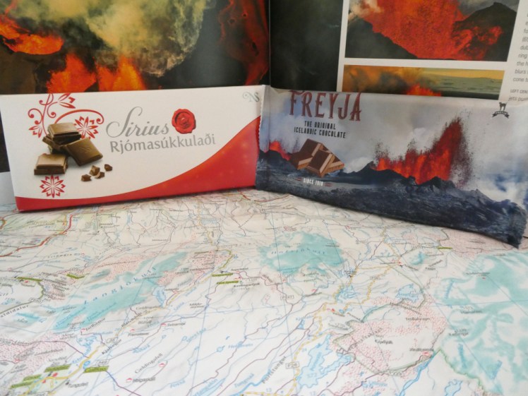 A bar of Sirius milk chocolate in a red and white cardboard box, and a bar of Freyja in packaging with a volcano on the front, both leaning against the big volcano book.