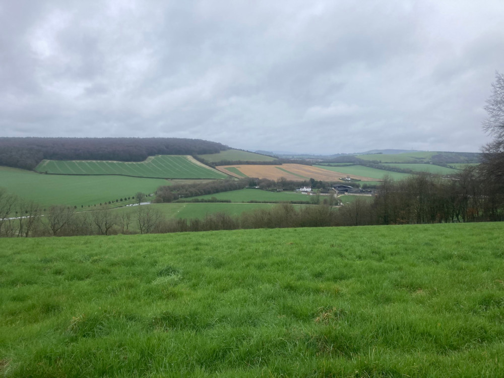 A very green valley with fairly steep sides although shallow enough to stretch across the entire view. In the bottom are some buildings and lakes. This is the end of my hike but it's still an hour away.