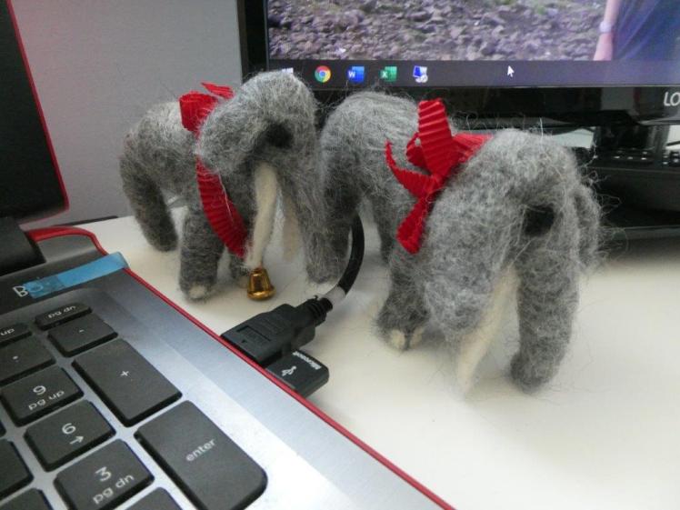 A pair of grey needle felted elephants wearing gold bells on red Lindt ribbons around their necks.