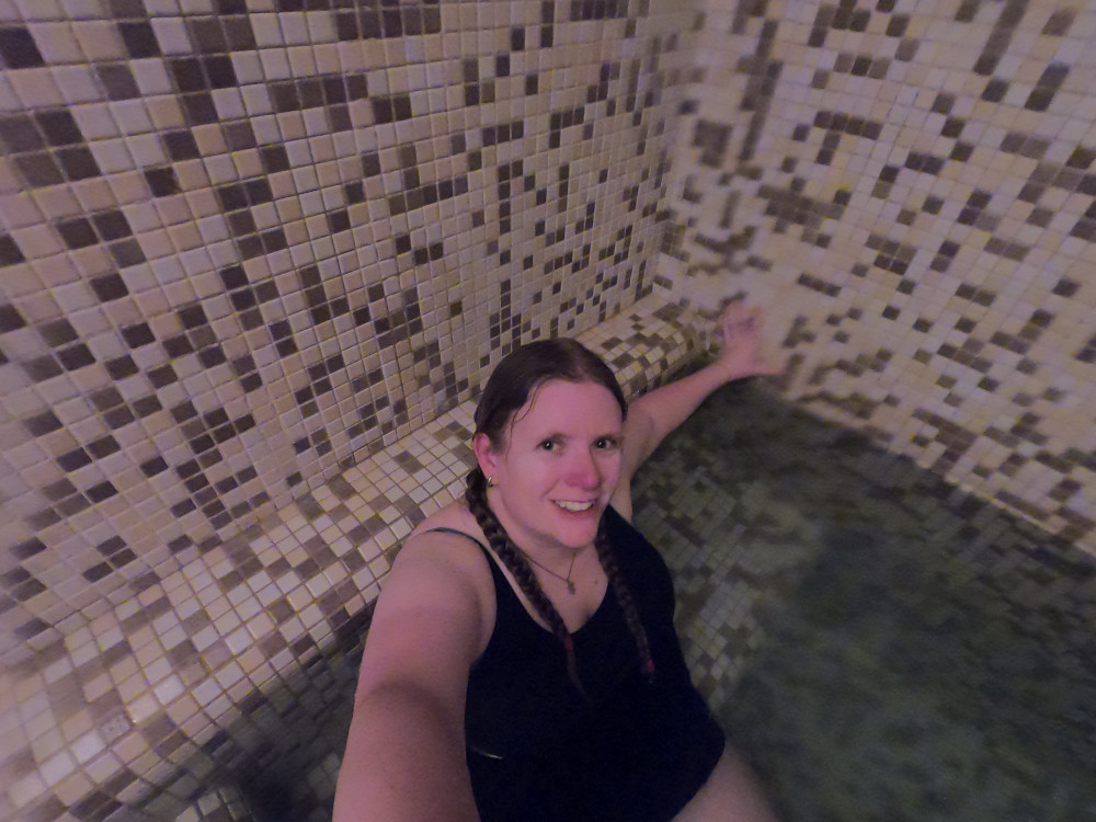 Me in an underlit sulphur bath wearing a navy blue one piece swimsuit with tiny inbuilt short legs.