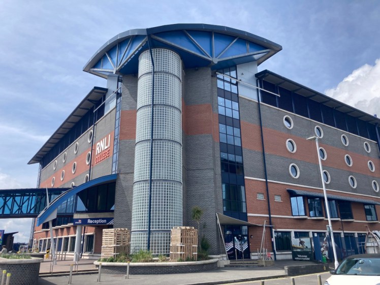 The RNLI College, a building in wide grey and red brick stripes. Most of the windows are circular and there's a glass stairwell running up the outside.
