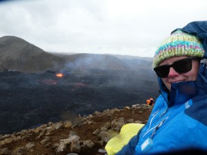 A selfie in the rain, sitting on the hillside with my sunglasses, hat and waterproof hood up, with the volcano looking very small in the background.
