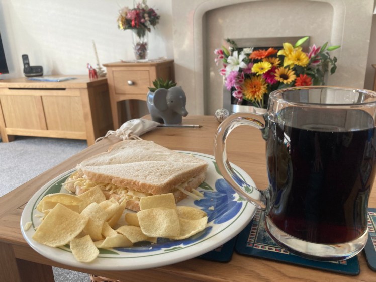 Home pub lunch: a cheese sandwich cut into triangles with Square crisps on the plate. Next to it is a pint mug of Coke.