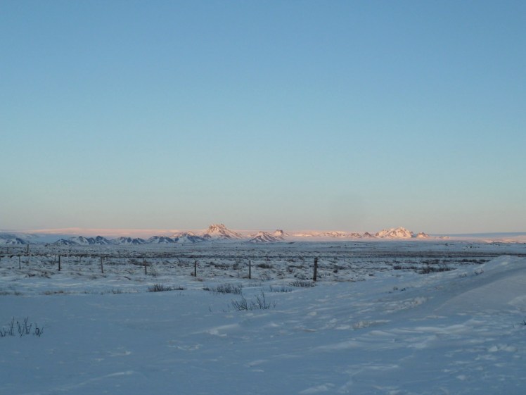 Langjokull glows in pink sunlight on the horizon, a sea of ice in the distance contained behind a few low rocky peaks.