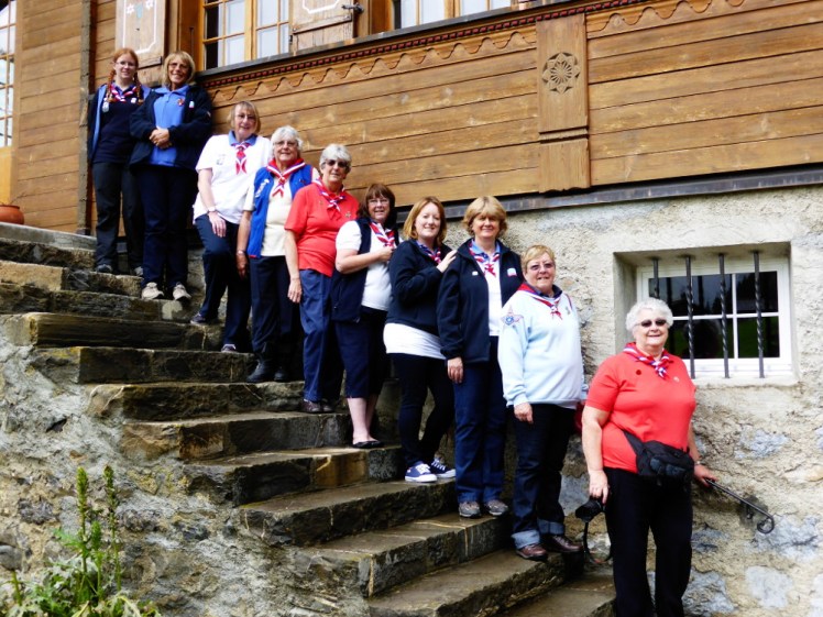 Group photo of the 2014 county group standing on the stone back steps of Our Chalet. We're in "uniform", which ranges from white to dark blue via light blue and red and no two people are dressed alike.