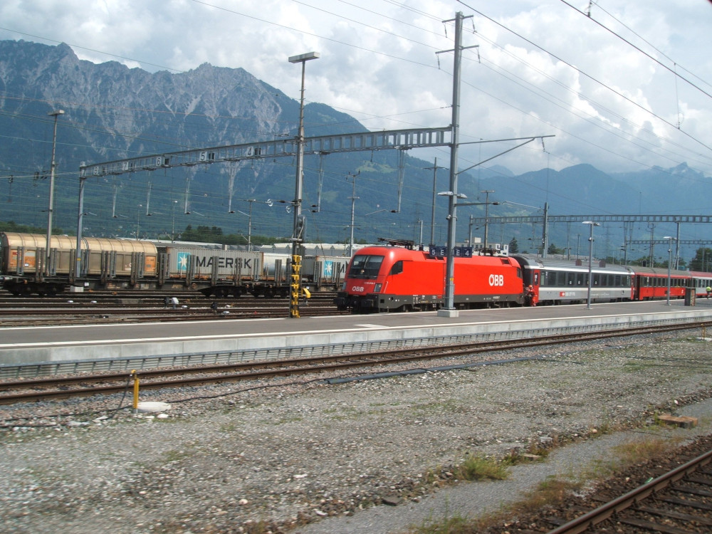 Chur station, an unlovely expanse of railway tracks, overhead wires, cargo wagons and in the middle, a large red electric OEBB locomotive pulling a red and grey train most likely bound for Austria.