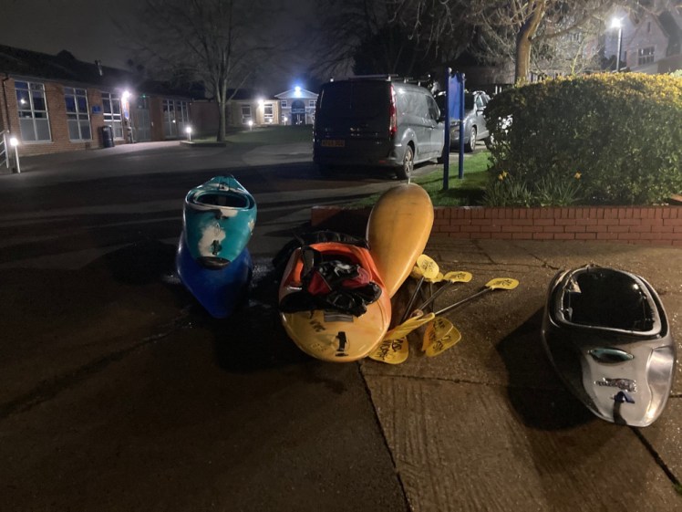 Some of the kayaks lying on the ground outside the pool, waiting to be put in the van. It's dark with a floodlight coming from the right. There are four kayaks, two of them the short kind that seem to be used for whitewater. Mine is the yellow one upside down in the middle.