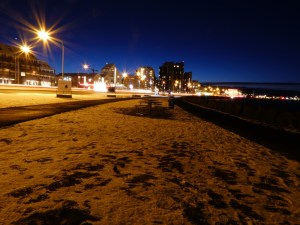 Long-exposure photo of downtown Reykjavik by night, all deep blue sky and orange-yellow streetlights, windows of small tower blocks and moving cars.