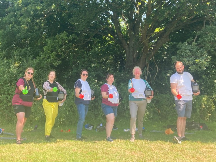 Six people in fencing jackets, standing under a tree holding plastic swords towards the camera. You can tell how hot it is from the fact that the sun has turned the green grass in front of us to glorious blazing golden yellow which is messing up the camera a bit.