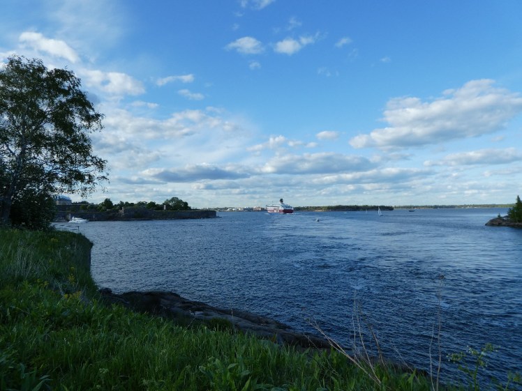 The ferry well out of reach of Suomenlinna, making its way into the city. The sky is blue but there's something about the light that says evening is approaching.
