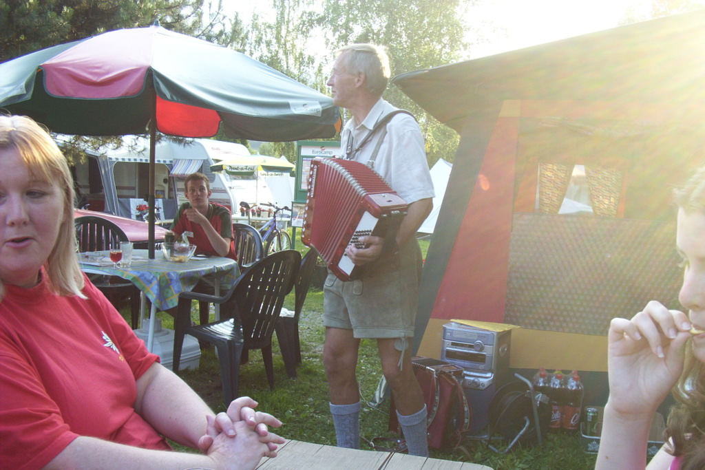 A glimpse of a Eurocamp tent and courier at a joint party in 2004. The Eurocamp tent is red and green, as is the umbrella and the uniform of the Eurocamp courier. The Keycamp courier is wearing Austrian traditional dress and playing an accordion