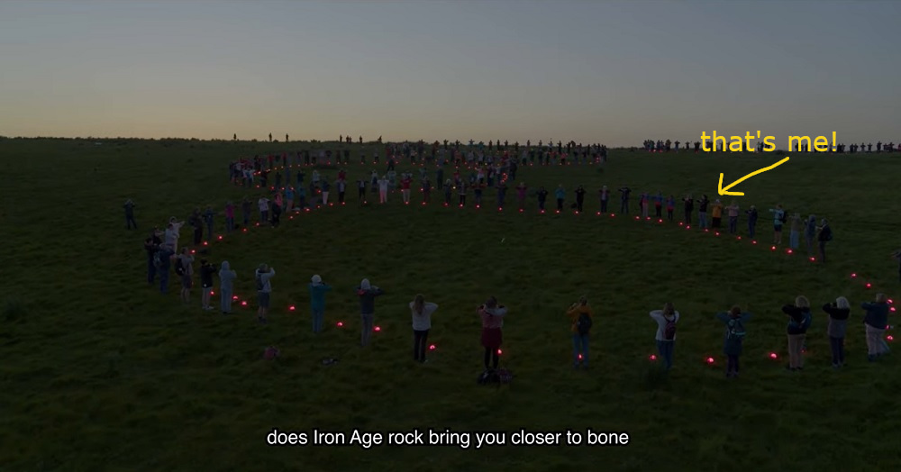 A screenshot from the short film, showing a circle of people holding pink lights in the dim twilight. I've drawn a yellow arrow pointing at a figure in a yellow jumper and it's labelled "that's me!".