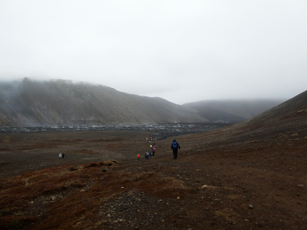 My first glimpse of the new lava! At the foot of the mountains, under the low cloud, is a sea of black lava. The surface is rippled with white and it's giving off columns of steam.