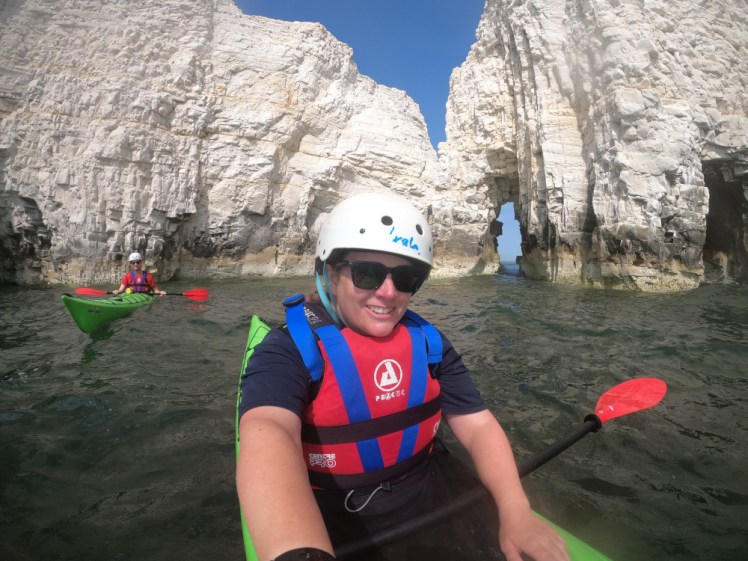 Bobbing around in a secret cove within Old Harry. Chris is visible behind me and behind us both are chalk cliffs with arches and cracks in them.