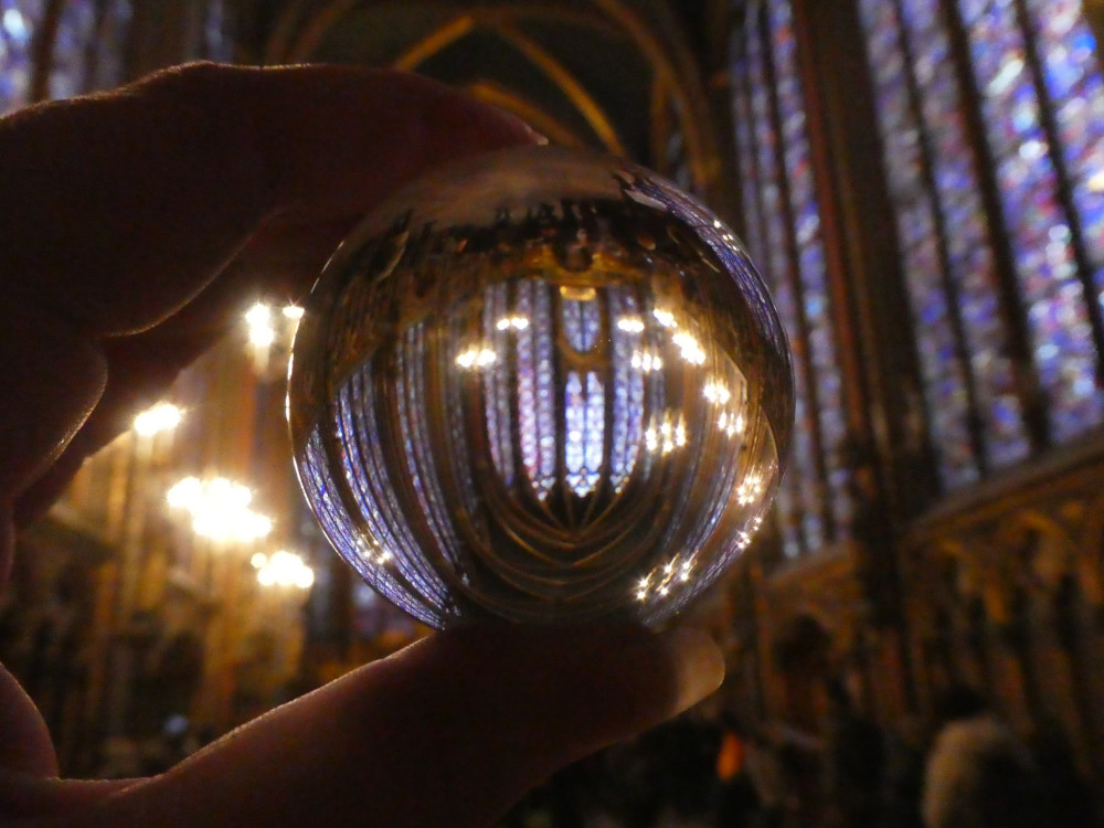 A glass ball a couple of inches in diameter held up to the camera. Inside it, you can see the tall Gothic-shaped red and blue stained glass windows of Sainte-Chapelle's upper chapel.