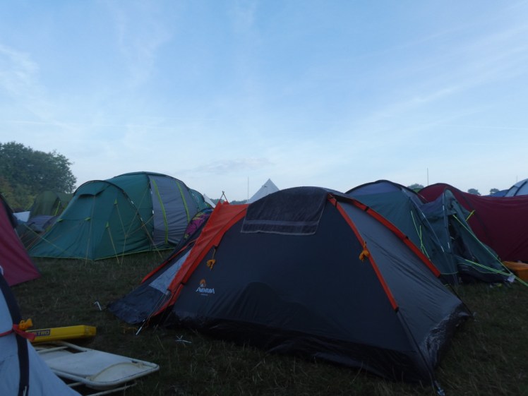 Lots of tents in various shapes, sizes and colours squashed together in a field. The sky is still blue but the field is noticeably getting dark.