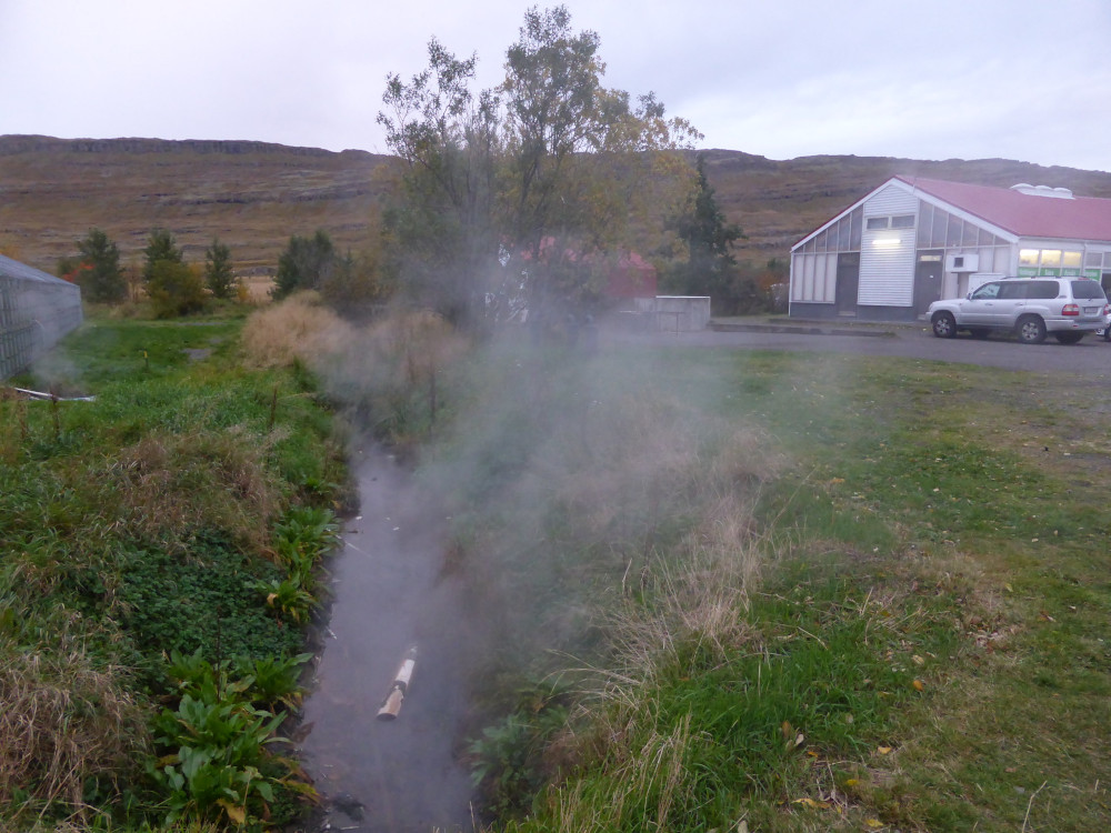 A steaming stream in a green field. Behind it is a building shaped like a greenhouse but with solid walls. Inside is a rural restaurant.