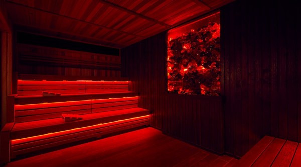 Lava Sauna: a dark sauna lit in red lights. The wooden benches glow red, as does the wall decoration, lots of red, black and transparent rocks behind a pane of glass.