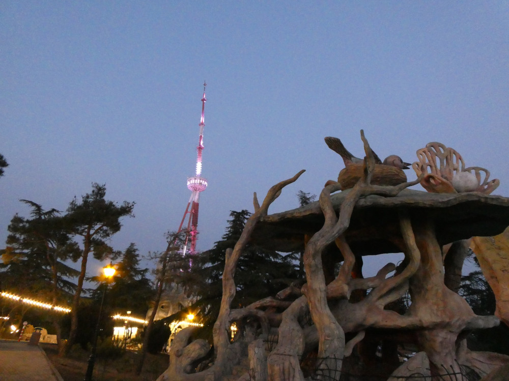 Tbilisi's TV tower, lit up in purple but still light enough to see that it's red and white, looms over a kind of fake wooden tree structure. This is by the entrance to Mtatsminda Park and it's where I took the previous selfie.