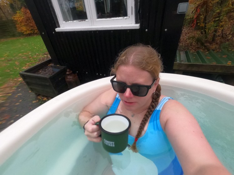 Me in a polar bear swimsuit, seen from above, sitting in the hot tub in daylight, drinking from an enamel mug.