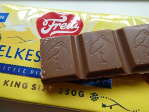 Three chunks of Freia chocolate with cranes embossed on them, lying on top of the packaging, which is yellow and shiny plastic.