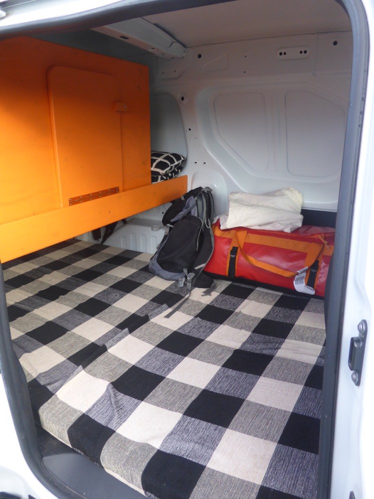 Inside my small campervan. The floor is a mattress and there's an orange wooden shelf