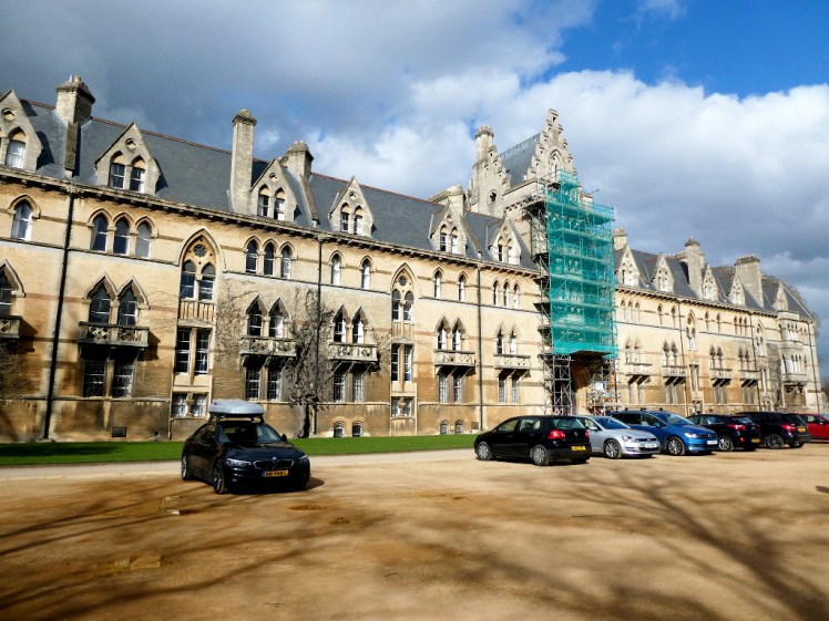 The visitors' entrance facade of Christ Church Oxford. A long row of yellow stone decorative buildings with scaffolding over the main entrance arch.