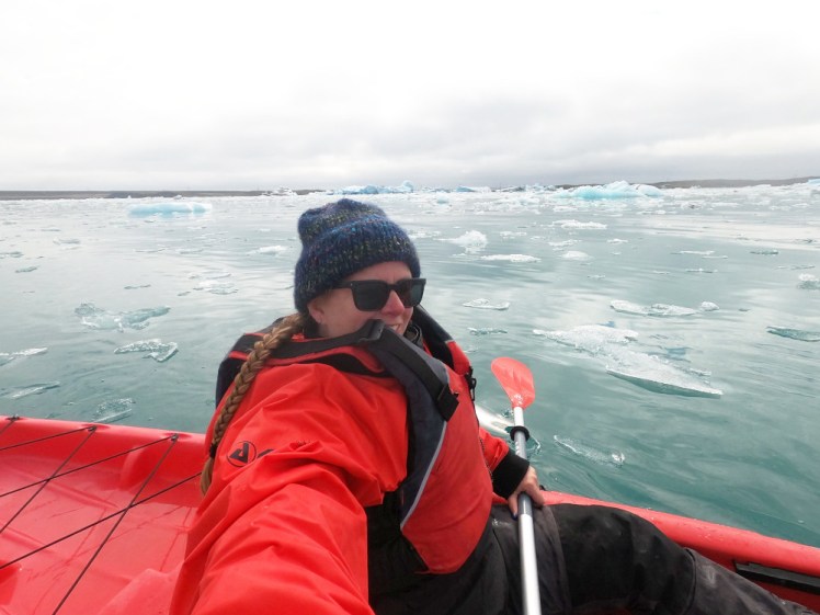 A selfie in the kayak. My buoyancy aid has slipped upwards a bit and is partly covering my face. What you can see of me looks very happy. Again, the background is all turquoise and white with icebergs and the glacier in the distance.