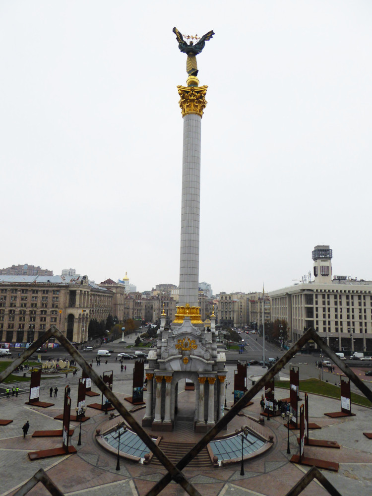 Another view of Maidan Nezalezhnosti, this time from the other end, below the glass arc of the shopping centre. The tall Ukraine Independence Monument, with the women holding the leaves aloft, is front and centres. Behind it are the heavy stone buildings down each side of the northern end.