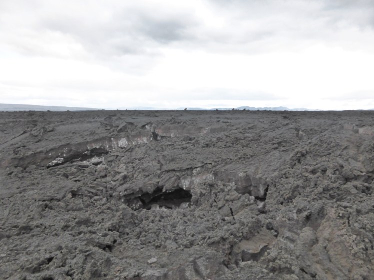 Holuhraun, a mass of grey lava that looks like it's recently been very sticky. It's visibly sharp now in places and there are holes. In the distance, you can see the expanse of a huge glacier gleaming on the horizon although it blends in a bit with the white sky.