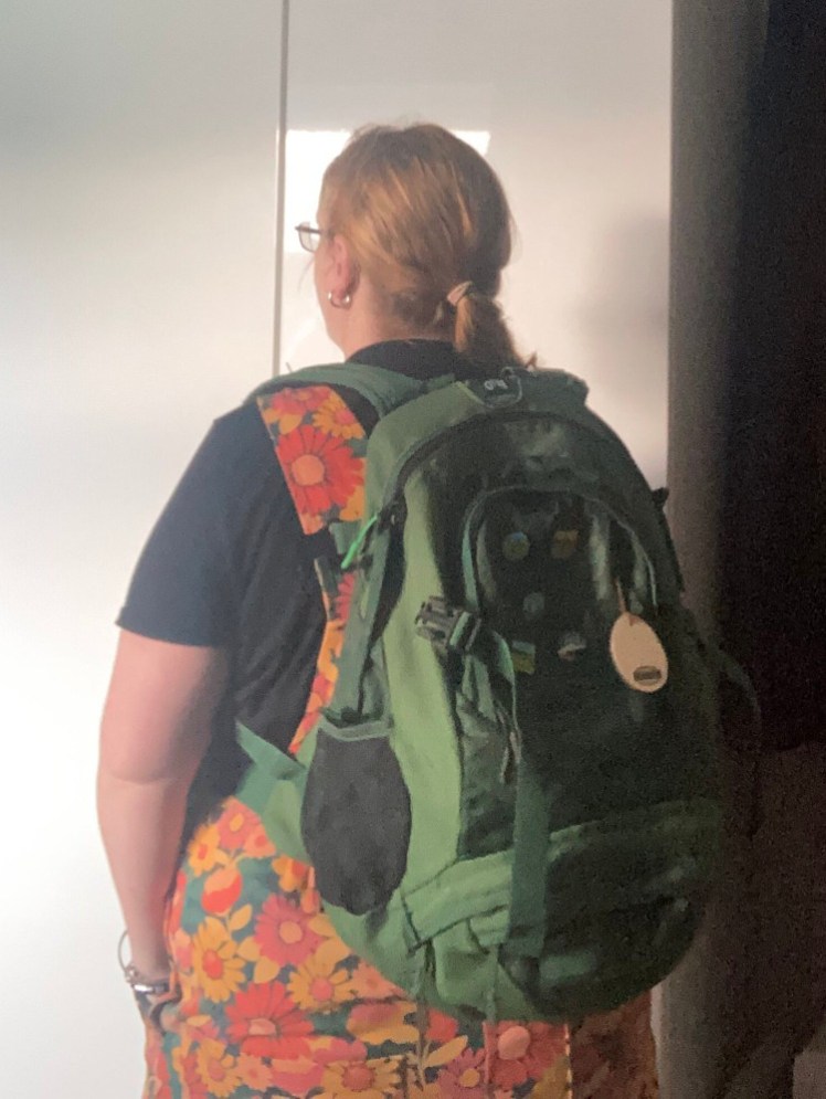 Me, in orange flowery dungarees, with my back to the camera so you can see the green backpack I'm wearing. It's fairly small, with compression straps unclipped and a pocket on the front.