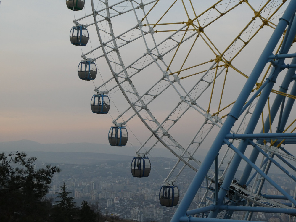 A hint of hazy pinkish grey sunset behind the bottom quarter of the big wheel, with Tbilisi just about visible below.