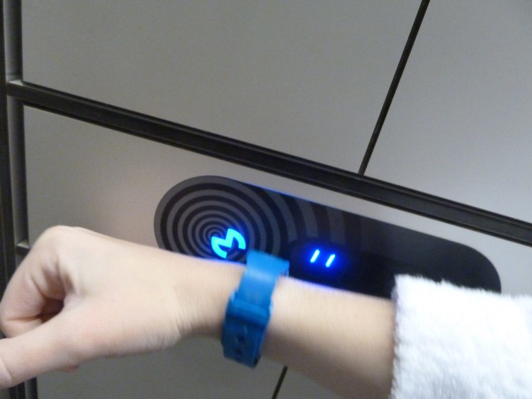 Using the Blue Lagoon wristband to lock my locker. A blue plastic wristband pressed to a contactless control panel.